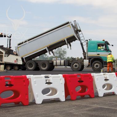Red and White Alphabloc barriers linked together in a line on site with tipper lorry in the background