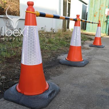 Black and yellow telescopic demarcation poles linked to orange and white traffic cones in a line